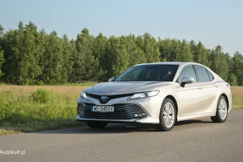 Elegancka Toyota Camry 2025 w kolorze szampańskim na tle zielonego krajobrazu.