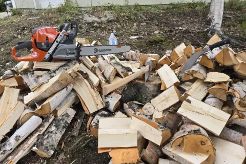 Piła łańcuchowa Husqvarna i siekiera leżą na stercie drewna. Do pracy przyda się olej Motul 800 2T do piły.