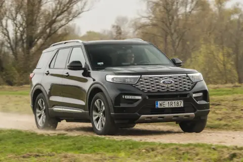 Czarny Ford Explorer 4x4 pokonuje piaszczystą drogę wśród drzew.