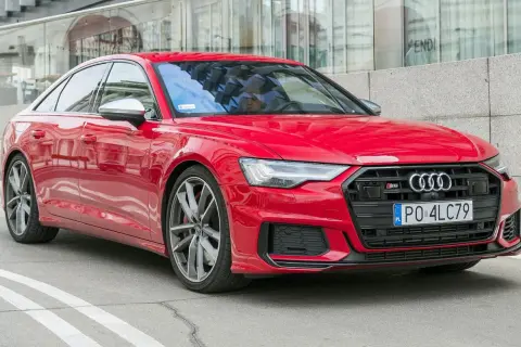 Czerwone Audi S6 C8 z polskimi tablicami rejestracyjnymi, zaparkowane przed nowoczesnym budynkiem z lustrzaną fasadą.