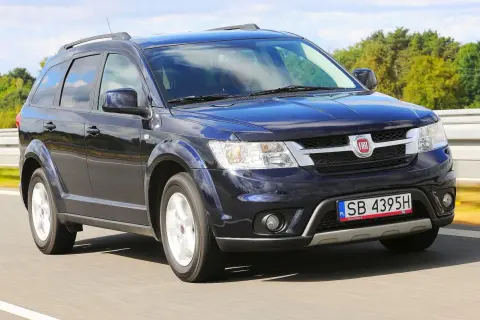 Ciemnoniebieski Fiat Freemont w ruchu drogowym. Wiele osób szuka o nim opinii, bo to praktyczny SUV.