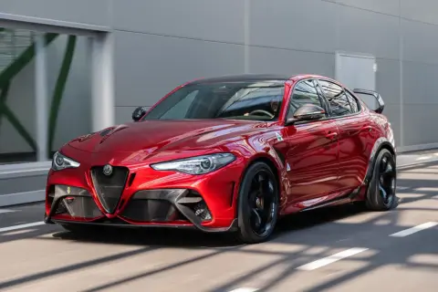 Czerwone Alfa Romeo Giulia GTAm z czarnym spojlerem i felgami pędzi po drodze.