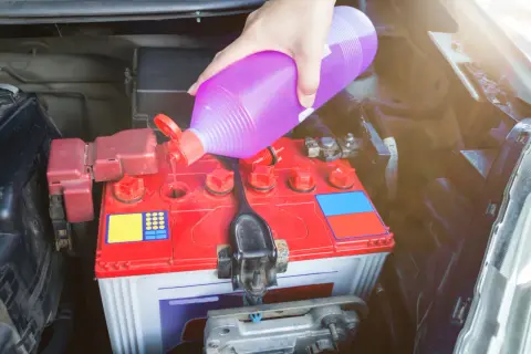 Ręka wlewa elektrolit do akumulatora samochodowego. Dbałość o stan techniczny pojazdu.