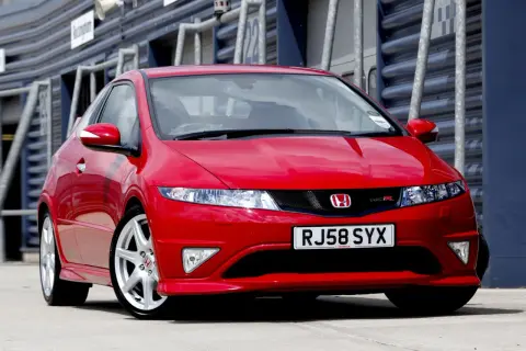 Czerwony Honda Civic Type R, wyglądający jak futurystyczne UFO, zaparkowany na torze wyścigowym.