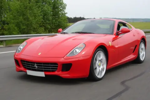 Czerwone Ferrari 599 pędzi po drodze, otoczone zielenią.