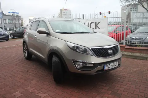Złoty Kia Sportage 2012 na czerwonej kostce brukowej, z tablicą rejestracyjną RZ 7652L.