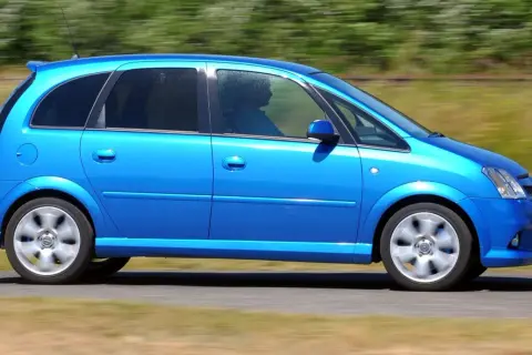 Błękitny Opel Meriva 1.4 benzyna w ruchu, z widocznym kierowcą za przyciemnianą szybą.