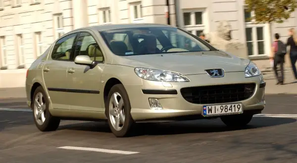 Złoty Peugeot 407 2.0 HDI jedzie ulicą.