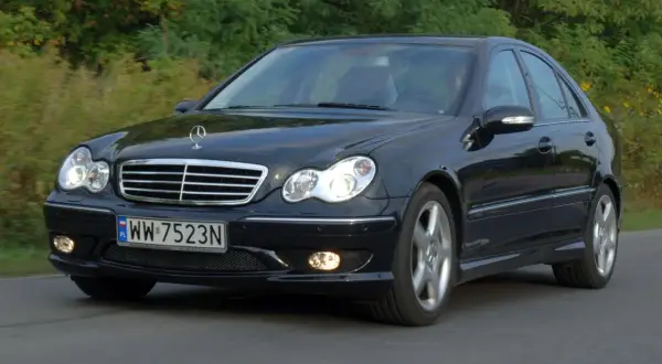 Czarny Mercedes-Benz w203 z tablicą rejestracyjną WW 7523N jedzie po drodze wśród zieleni.