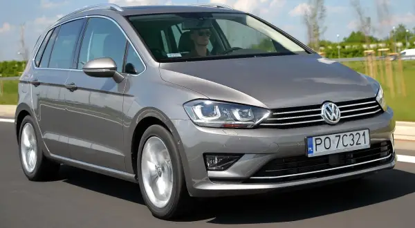 Szary Volkswagen Sportsvan jedzie po drodze. Kierowca w okularach prowadzi auto.