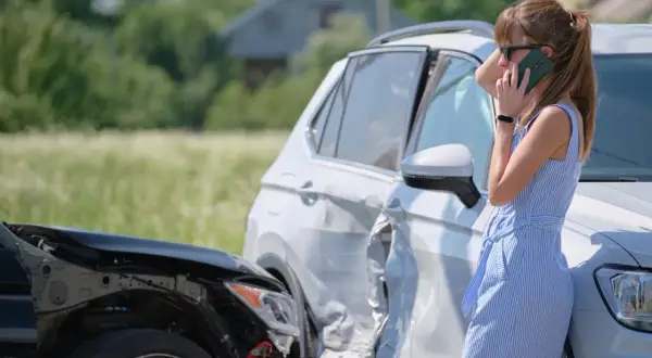 Kobieta rozmawia przez telefon obok dwóch uszkodzonych samochodów po kolizji.