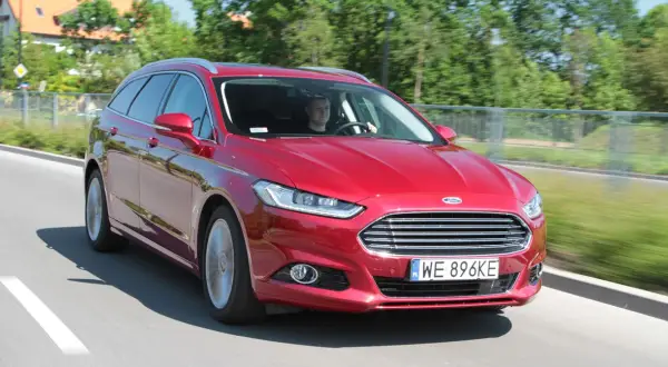 Czerwony Ford Mondeo MK4 kombi w ruchu drogowym. Kierowca uśmiecha się, a opinie o tym modelu są zazwyczaj pozytywne.