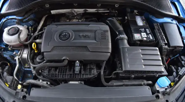 Silnik 1.8 TFSI w samochodzie Skoda. Widoczny jest blok silnika, akumulator, obudowa filtra powietrza i zbiornik płynu chłodniczego.