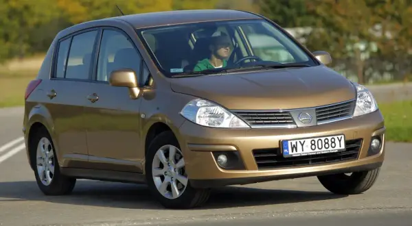 Złoty Nissan Tiida z mężczyzną za kierownicą jedzie po drodze.