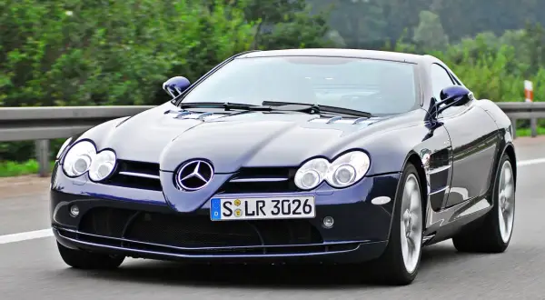 Granatowy SLR McLaren pędzi po autostradzie, otoczony zielenią.