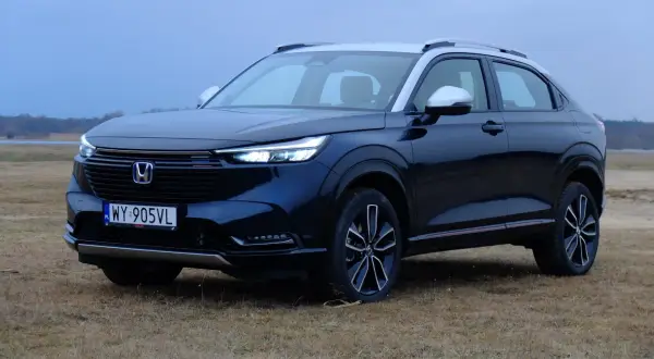 Ciemnoniebieski Honda HR-V na tle suchej trawy i jeziora.