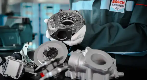 Mechanik w białych rękawiczkach prezentuje części turbosprężarki. W tle logo Bosch Service.