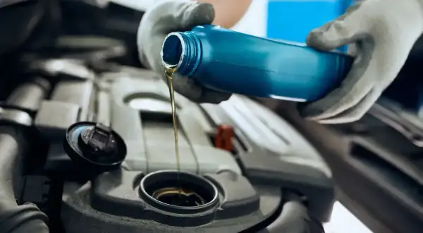 Ręce w rękawiczkach wlewają olej silnikowy 5W30 do silnika. Czy to Motul czy Castrol?