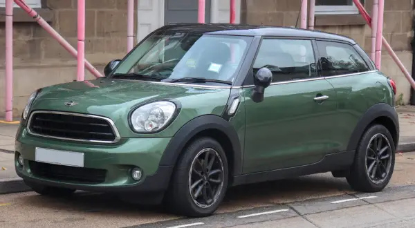 Zielony mini paceman z czarnym dachem stoi na ulicy, mokry od deszczu.