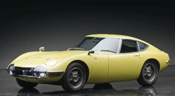 Żółta Toyota 2000GT z lat 60. prezentuje swoje klasyczne linie na błyszczącej podłodze.