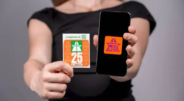 Kobieta trzyma winietę szwajcarską i smartfon z aplikacją e-winiety.
