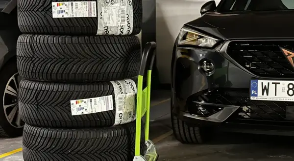 Cztery nowe opony Michelin CrossClimate 2 na wózku, gotowe do montażu w czarnym aucie. To najlepsze opony wielosezonowe dla pewności jazdy przez cały rok.