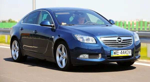 Niebieski Opel Insignia 2.0 Turbo pędzi po drodze, kierowca skupiony na trasie.