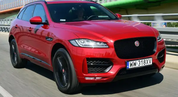Czerwony Jaguar F-Pace na drodze. Kierowca w środku. Wiele pozytywnych jaguar f pace opinie potwierdza jego styl.