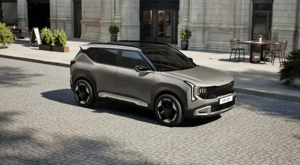 Nowy model Kia, szary SUV, parkuje na brukowanej ulicy przed eleganckim budynkiem.