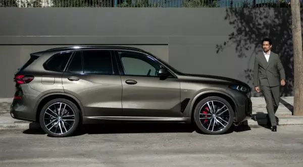 Elegancki mężczyzna w garniturze obok lśniącego BMW G05.