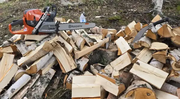 Piła łańcuchowa Husqvarna i siekiera leżą na stercie drewna. Do pracy przyda się olej Motul 800 2T do piły.