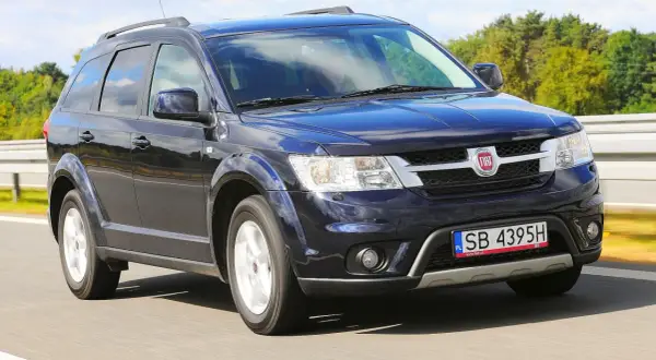 Ciemnoniebieski Fiat Freemont w ruchu drogowym. Wiele osób szuka o nim opinii, bo to praktyczny SUV.