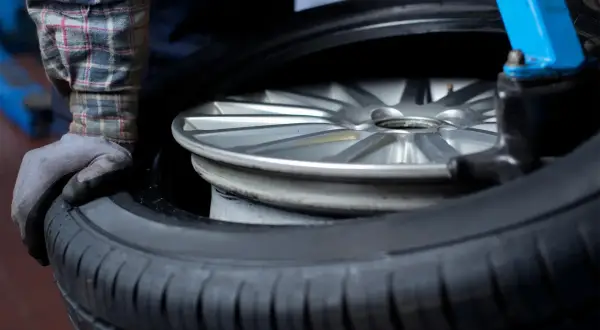 Mechanik w rękawiczce przygotowuje felgę do wymiany opony. Zastanawiasz się, ile kosztuje wymiana opon?