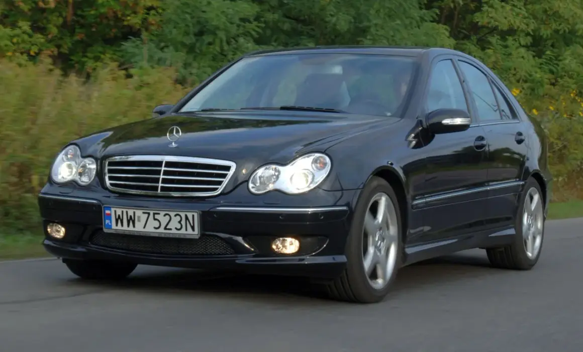 Czarny Mercedes-Benz w203 z tablicą rejestracyjną WW 7523N jedzie po drodze wśród zieleni.