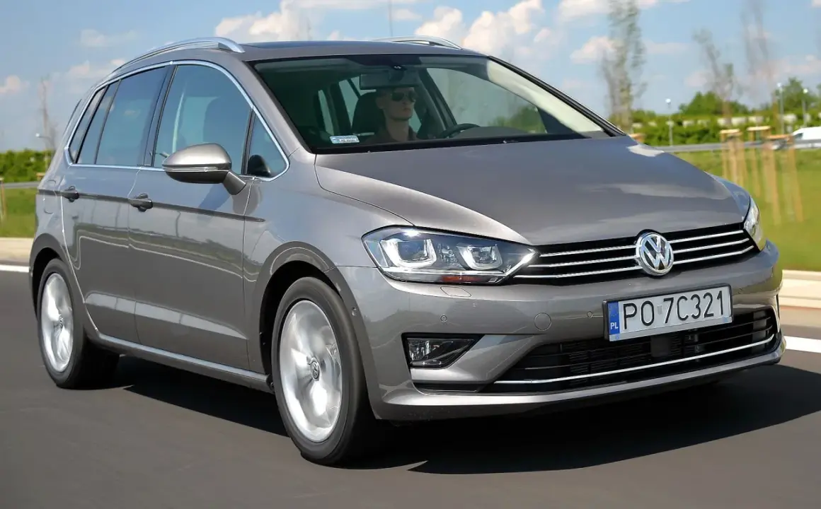 Szary Volkswagen Sportsvan jedzie po drodze. Kierowca w okularach prowadzi auto.
