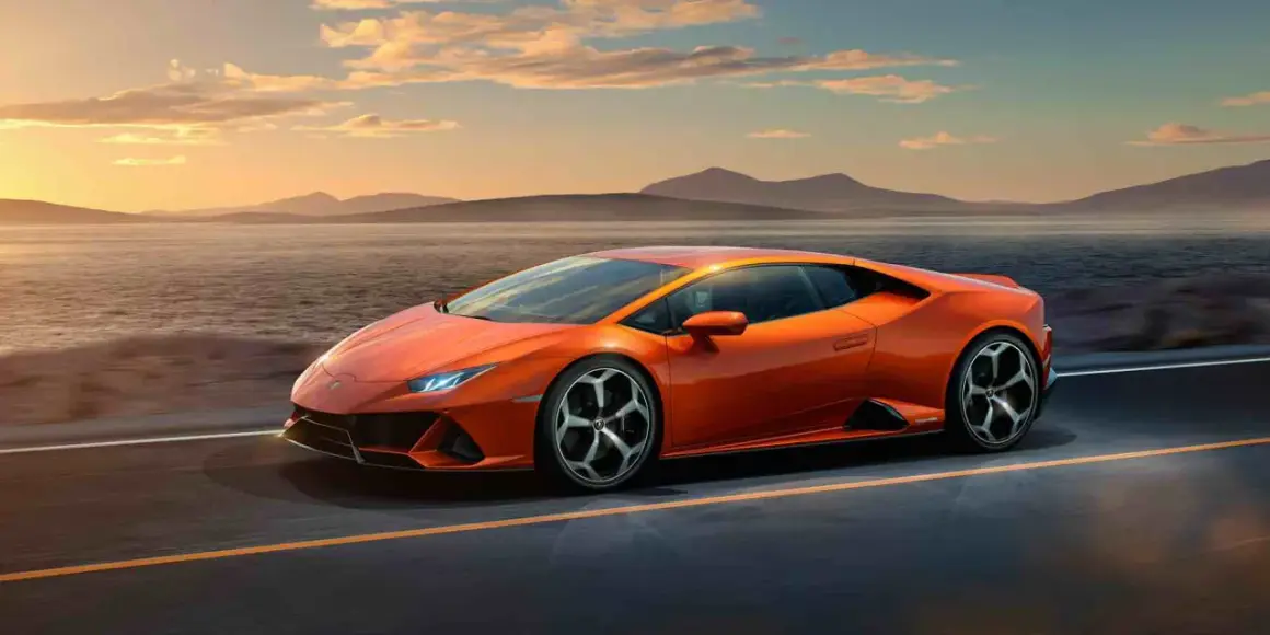 Pomarańczowy Lamborghini Huracan Evo pędzi wzdłuż malowniczego wybrzeża o zachodzie słońca.