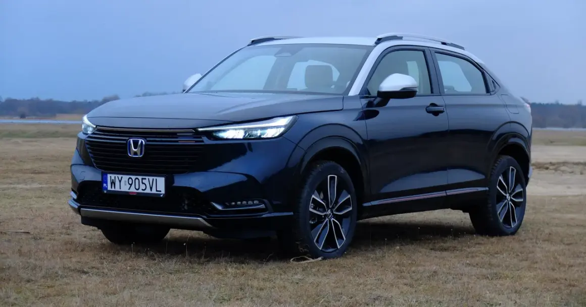 Ciemnoniebieski Honda HR-V na tle suchej trawy i jeziora.