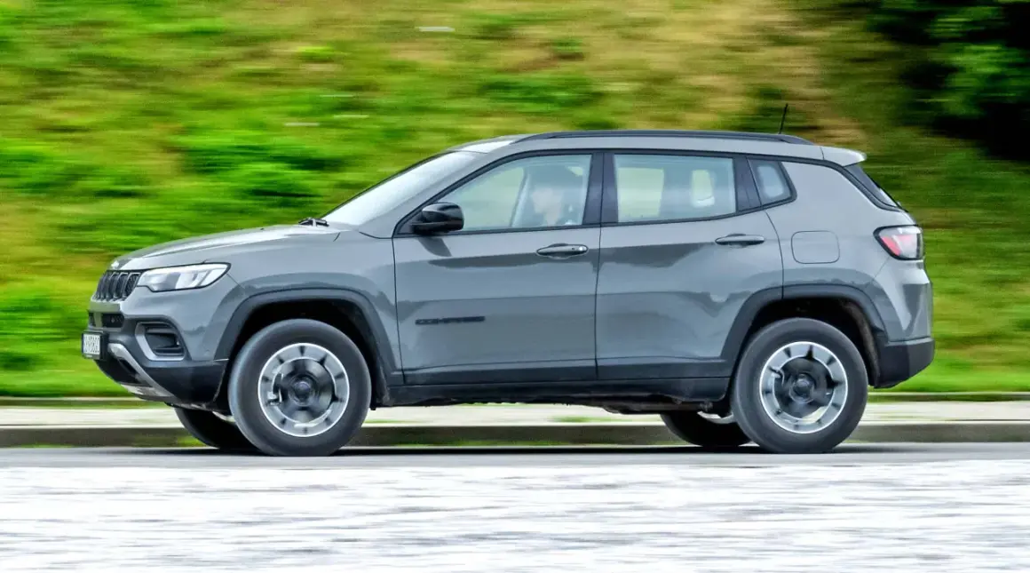 Szary Jeep Compass 4xe w ruchu, z rozmytym zielonym tłem.