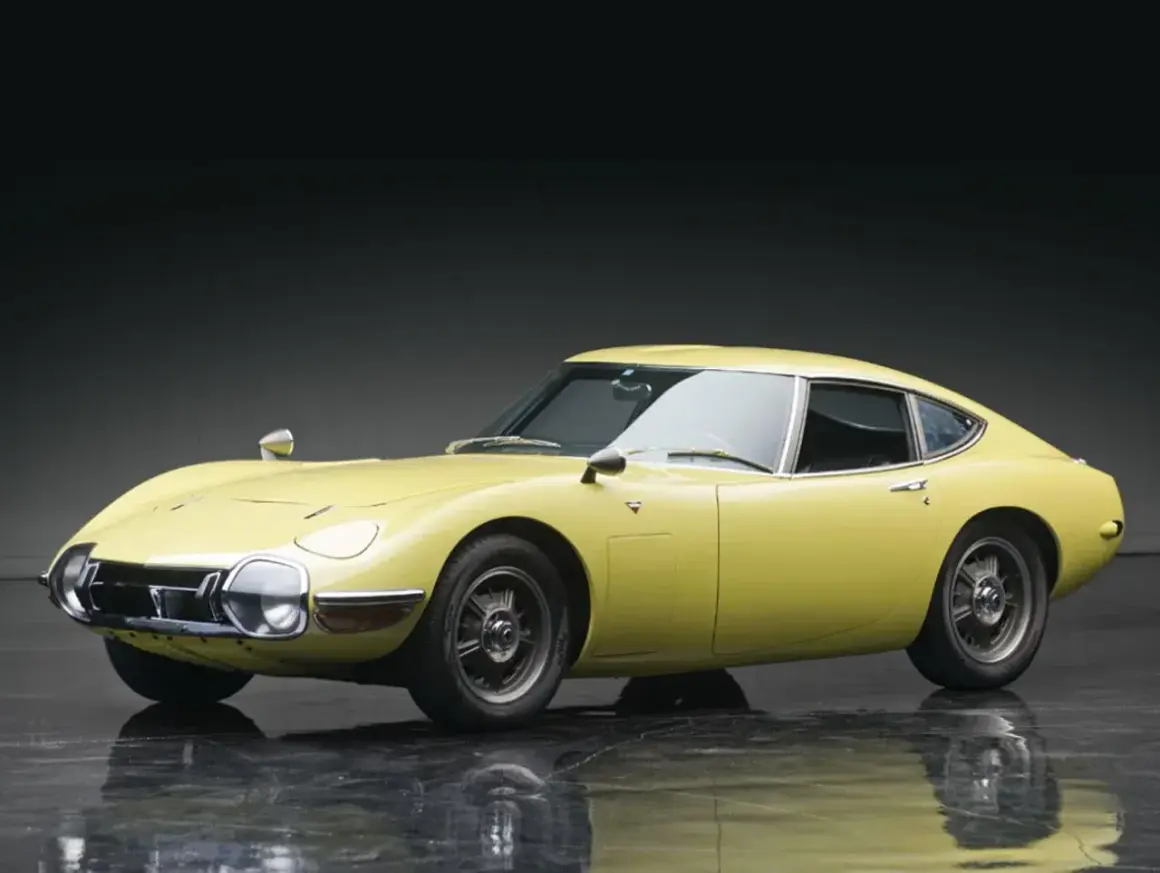 Żółta Toyota 2000GT z lat 60. prezentuje swoje klasyczne linie na błyszczącej podłodze.