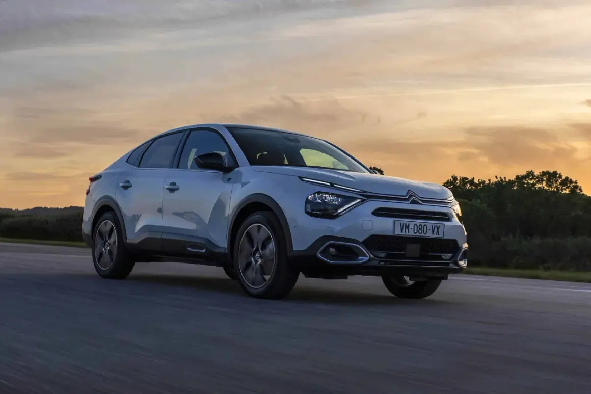 Jasnoszary Citroën C4X sunie po drodze podczas zachodu słońca.