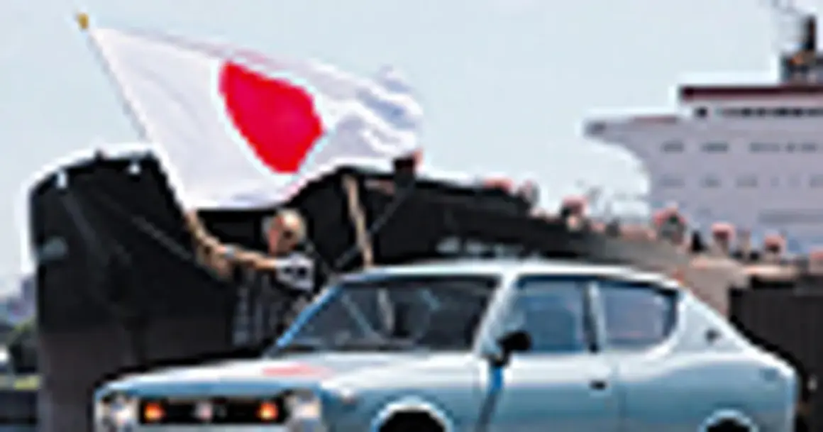 Jasnoniebieski Datsun 100A z flagą Japonii na tle statku.