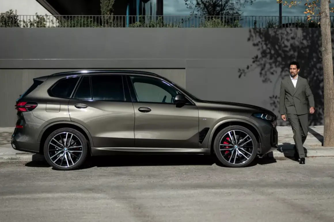 Elegancki mężczyzna w garniturze obok lśniącego BMW G05.