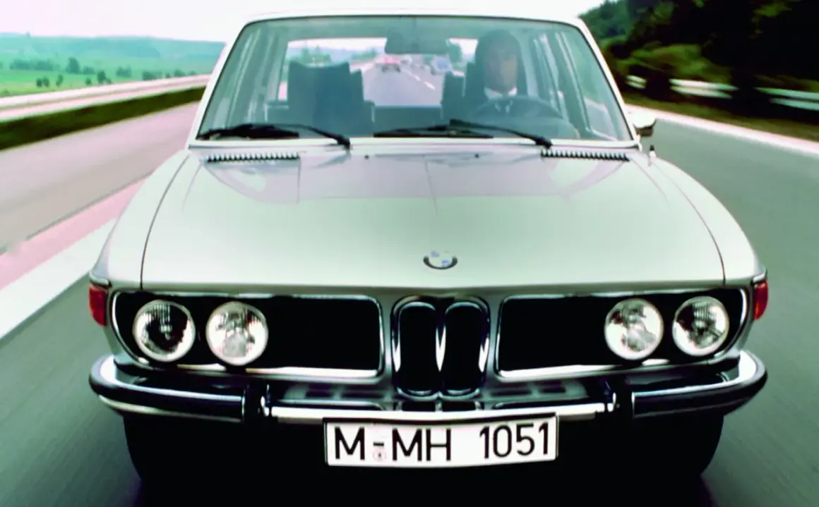 Klasyczne bmw e3 pędzi autostradą. Kierowca w garniturze pewnie prowadzi lśniący samochód.