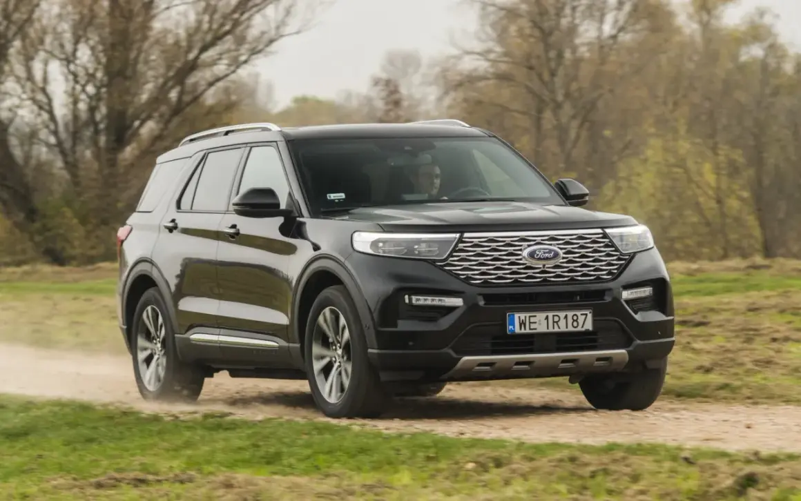 Czarny Ford Explorer 4x4 pokonuje piaszczystą drogę wśród drzew.