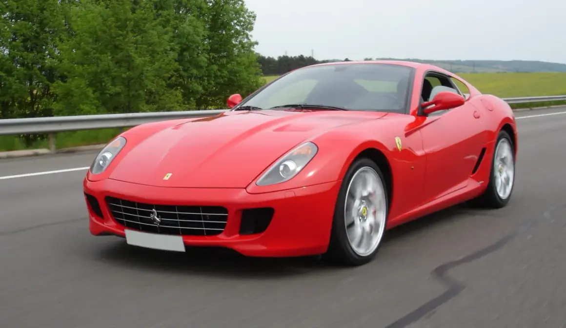 Czerwone Ferrari 599 pędzi po drodze, otoczone zielenią.