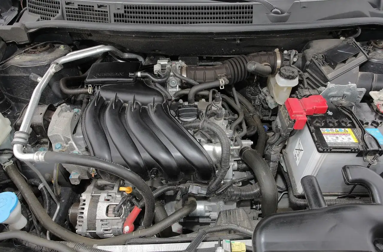 Silnik Nissan Qashqai 1.6 benzyna, widok komory silnika z akumulatorem i elementami układu dolotowego.