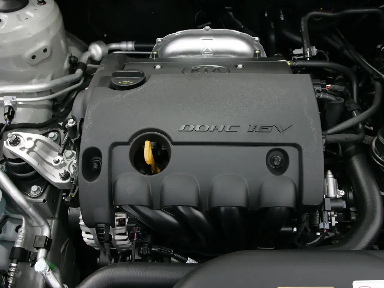 Silnik DOHC 16V w Kia Ceed 1.6 benzyna. Widoczny czarny plastikowy kolektor, żółta miarka oleju i elementy układu chłodzenia.