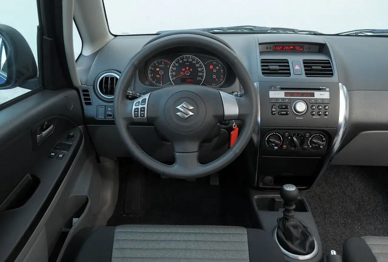 Wnętrze Suzuki SX4 1.6 benzyna: kierownica, deska rozdzielcza z radiem i zegarami, dźwignia zmiany biegów.