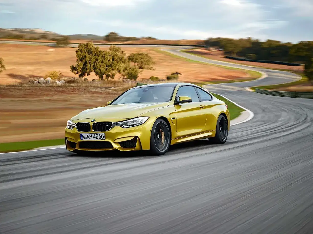 Żółte BMW M4 F82 na torze wyścigowym, pokonujące zakręt z dynamicznym ruchem.