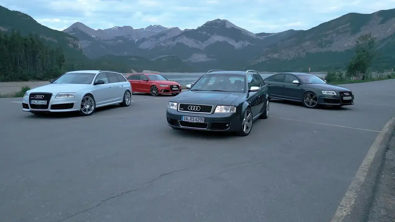 Cztery Audi RS6, w tym jeden sedan, zaparkowane nad jeziorem z górami w tle.